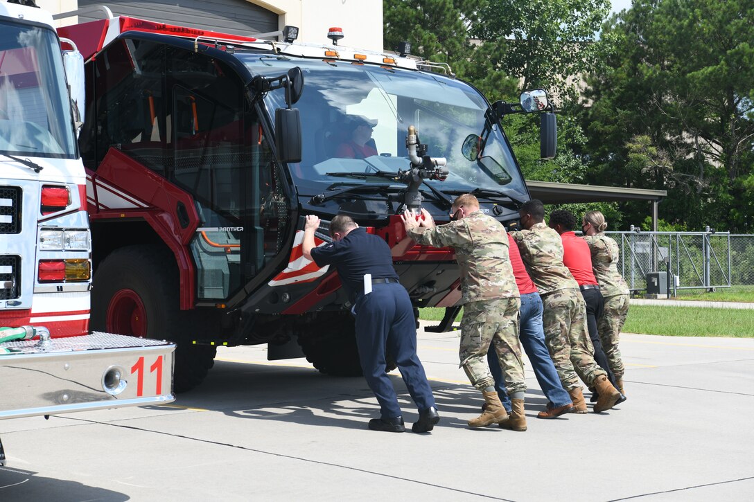 Photo shows group of six people pushing a fire truck backwards into its hangar while a person inside the truck is reversing it.