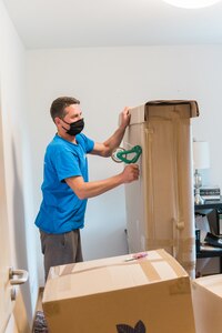 WIESBADEN, Germany - A mover tapes up a box at an apartment at U.S. Army Garrison Wiesbaden May 22 while following health protocols. The Department of Defense has directed that moving personnel adhere to Centers for Disease Control and Prevention protocols regarding health protection, such as wearing face coverings and washing hands, while working in a person’s home. (U.S. Army photo by Lisa Bishop)