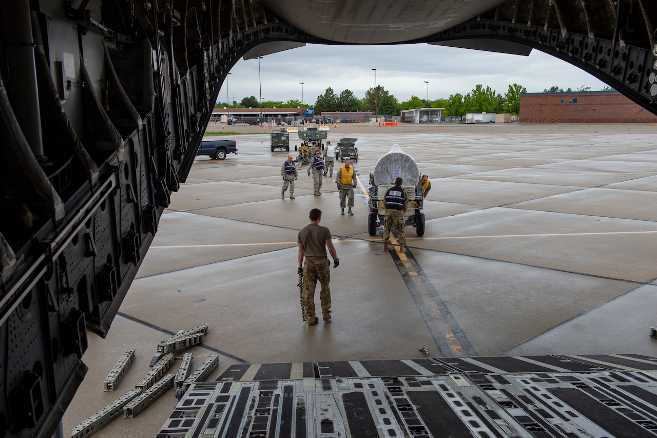Airmen working on a flight line as seen from inside a transport jet’s cargo bay.