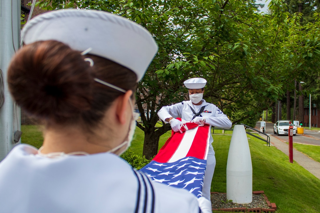 Two Navy officers wearing masks fold a flag.