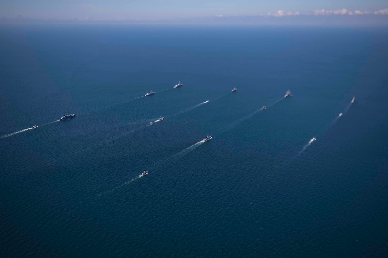 Ships of many nations steam in formation.