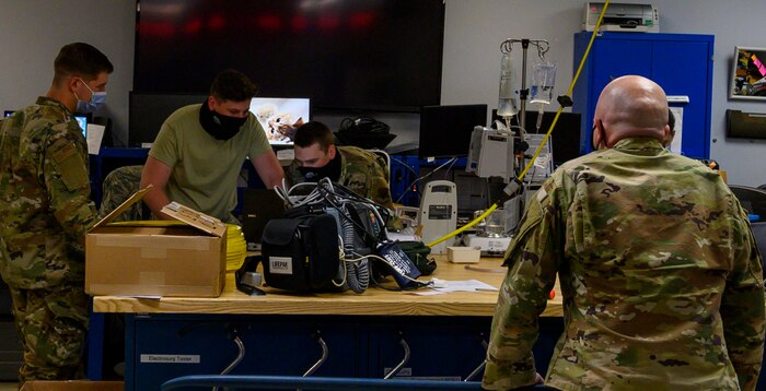 Three Airmen test an IV machine while one Airman supervises.