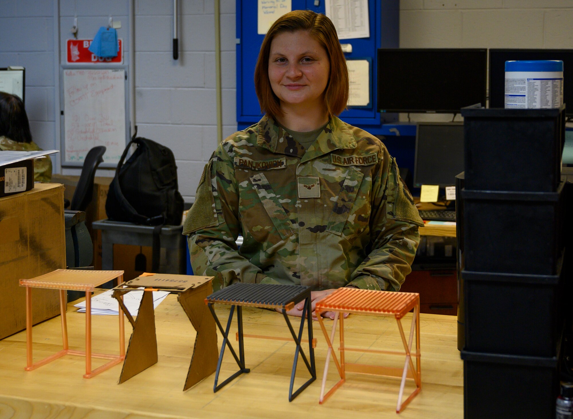 An Airman stands behind four prototypes of a curing rack the used for Nasopharyngeal swabs.