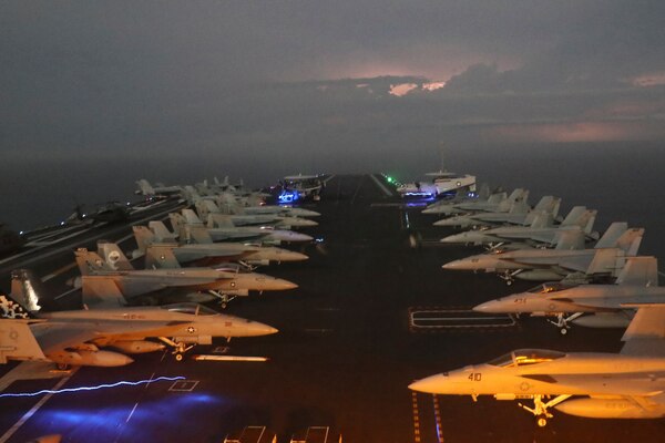 Military aircraft are lined up on the deck of an aircraft carrier during stormy weather.
