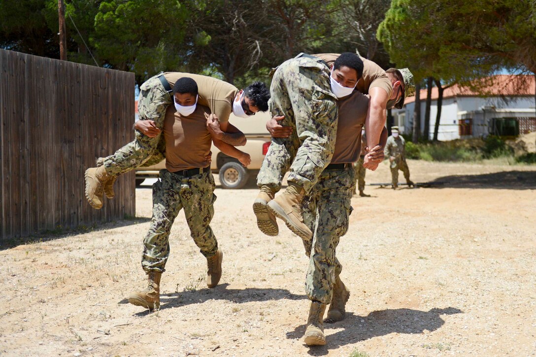 Two sailors carry two other sailors over their backs.