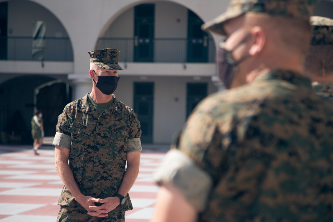 Marine Corps officer wearing a face mask speaks with young Marines.