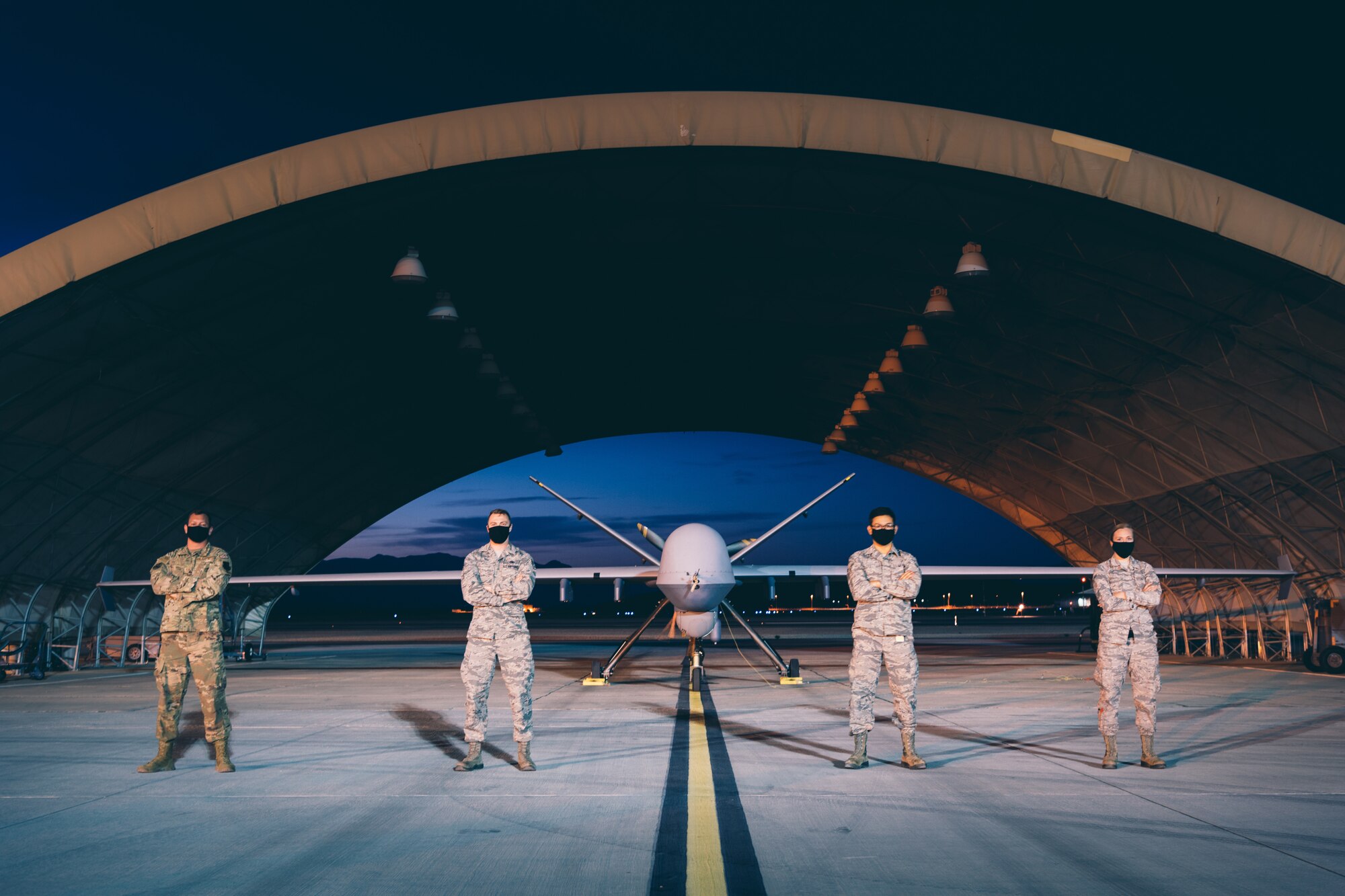 Four Airmen from the 432nd Aircraft Maintenance Squadron, Tiger Flight, stand in front of an MQ-9 Reaper at night.