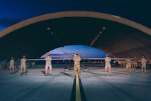 Airmen in protective masks, due to COVID-19, pose for a photo in front of an MQ-9 Reaper at night.