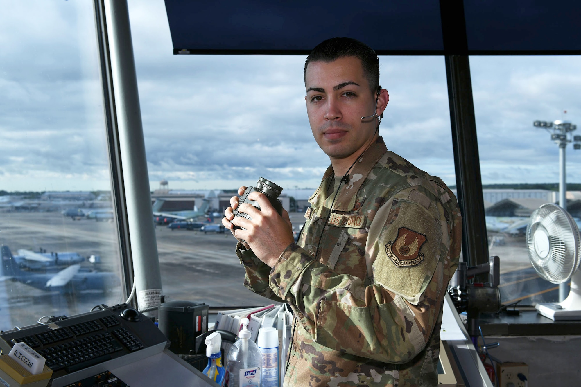 Photo shows an Airman standing inside the air control tower holding binoculars in his hands.