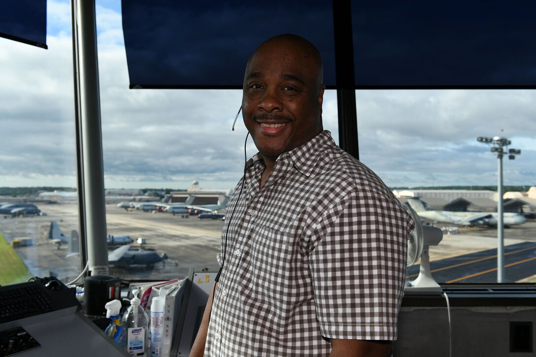 Photo shows a man smiling at the camera from inside the air traffic control tower.