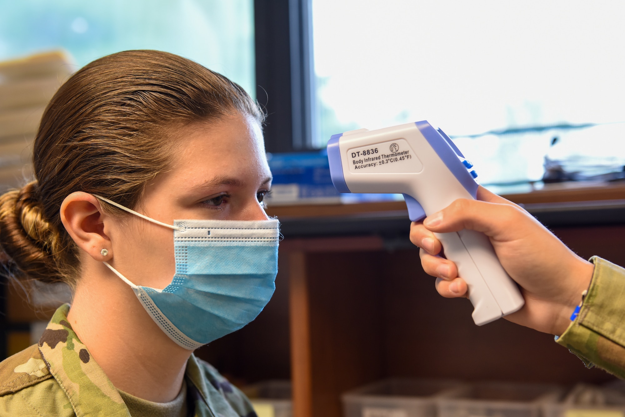 A public health technician takes the temperature of a fellow guardsman at the 171st Air Refueling Wing, Coraopolis, Pennsylvania, June 3, 2020. Masks are to be worn at all times except when isolated from others in private spaces. (U.S. Air National Guard photo by Senior Airman Zoe M. Wockenfuss)