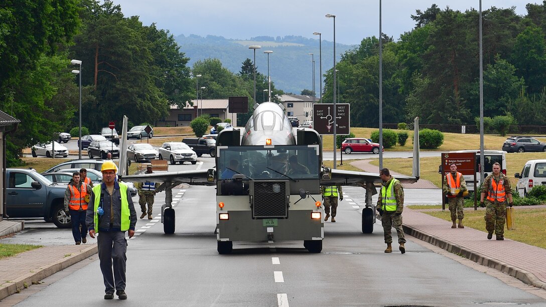 Workers walk beside a vehicle towing a jet aircraft.