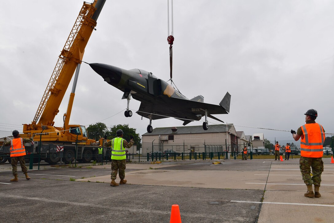 Airmen hold a jet aircraft being lifted by a crane steady with ropes.