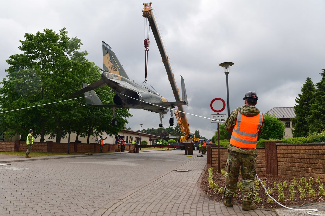 Workers hold a jet aircraft being lifted by a crane steady with ropes.