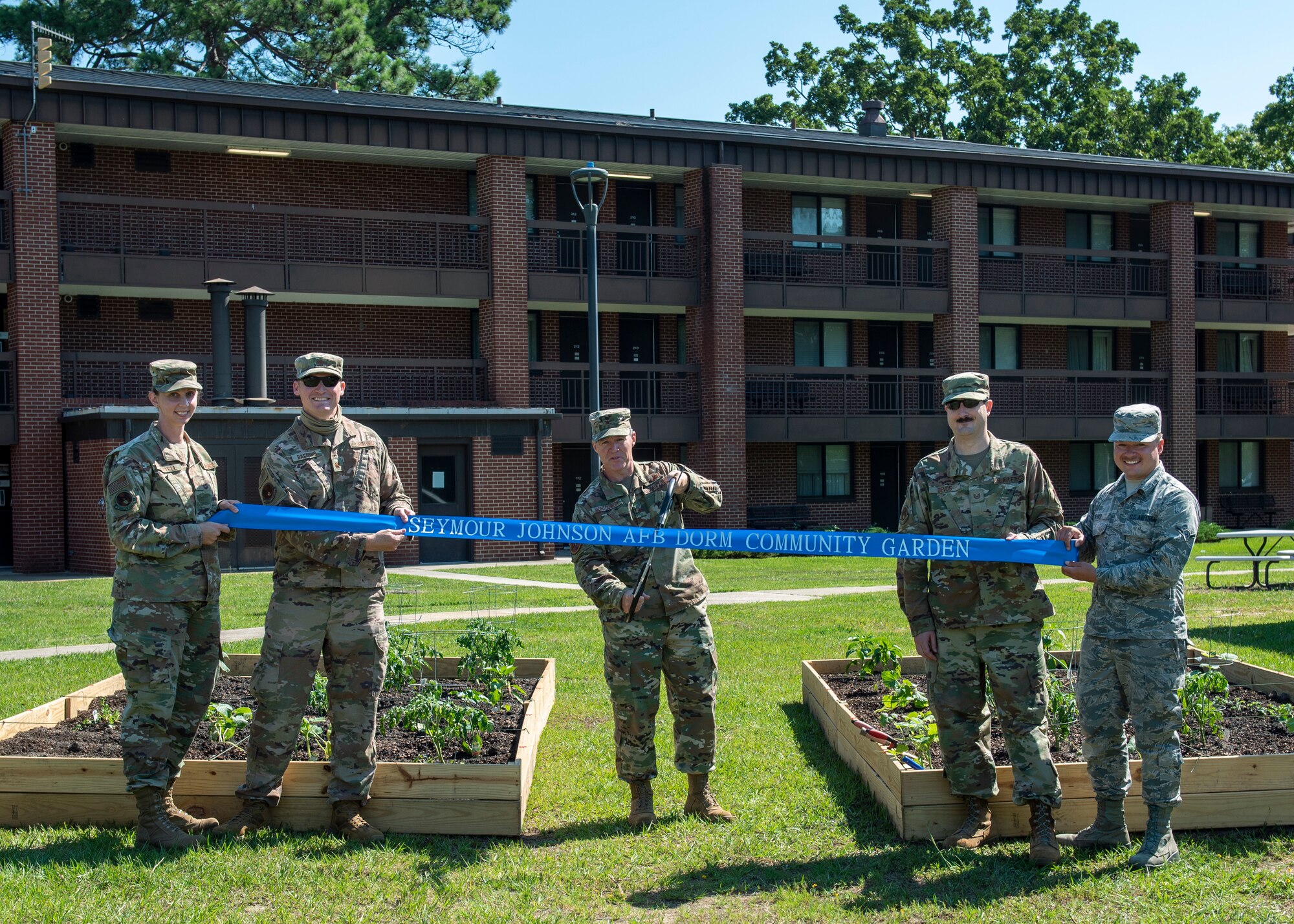 Col. Brian Montgomery, 4th Fighter Wing vice commander, center, and members of Team Seymour cut the ribbon at the opening of the Dorm Community Garden at Seymour Johnson Air Force Base, North Carolina, June 8, 2020.