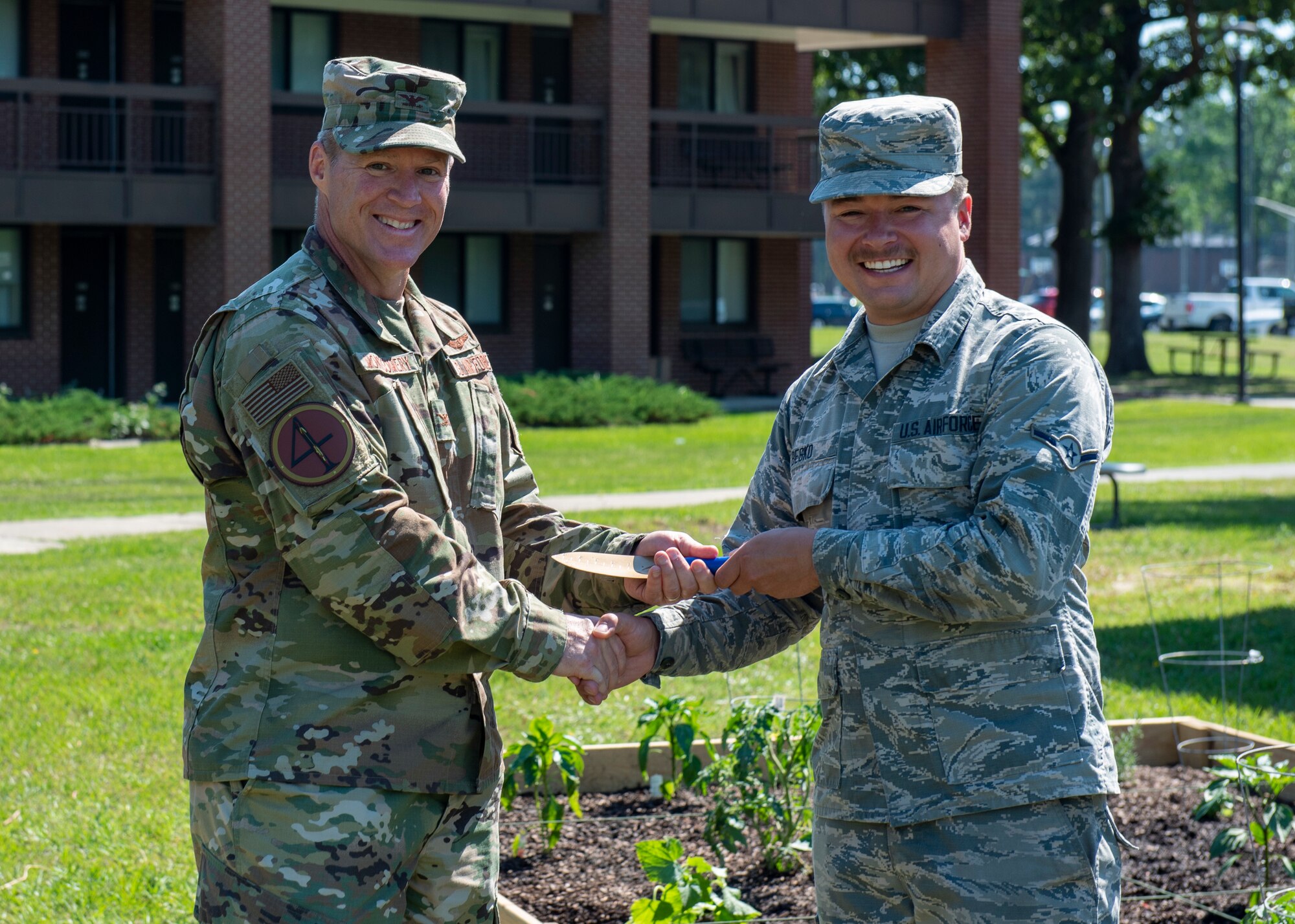 Col. Brian Montgomery, 4th Fighter Wing vice commander, left, hands a golden spade to Airman Joseph Besko, 4th Component Maintenance Squadron avionics technician, right, at the opening of the Dorm Community Garden at Seymour Johnson Air Force Base, North Carolina, June 8, 2020.