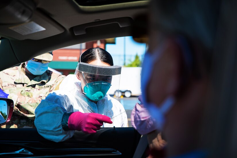 A National Guardsman wearing personal protective equipment administers a COVID-19 test in a drive-thru testing area.