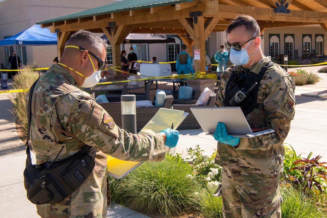 Two airmen wearing protective gear speak to each other.