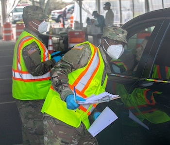 New York Army National Guard Spc. Shevon Reid assigned to the 107th Military Police Company,  53rd Troop Command, New York Army National Guard, alongside Spc. Jason Trinadad, 369th Sustainment Brigade HHC, 53rd Troop Command, gives instructions to people at a COVID-19 Mobile Testing Center in Glenn Island Park, New Rochelle, April. 4, 2020. The New York National Guard continues support at seven drive-thru testing sites. Soldiers and Airmen are collecting samples and providing general-purpose support at the testing locations, now exceeding 5,000 tests per day in total.