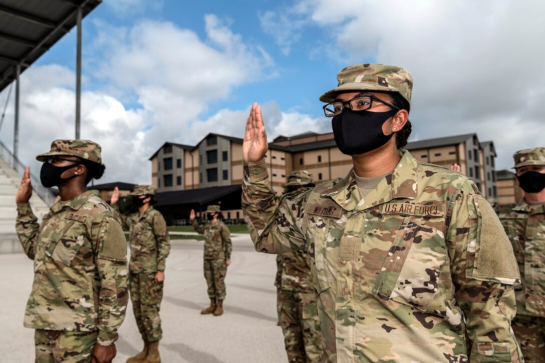 Airmen wearing masks stand several feet apart from one another and hold up their right hands.