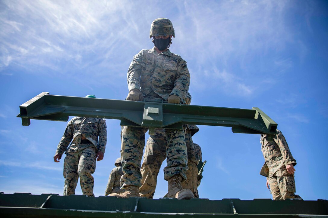 A Marine carries a large metal panel; others stand behind.