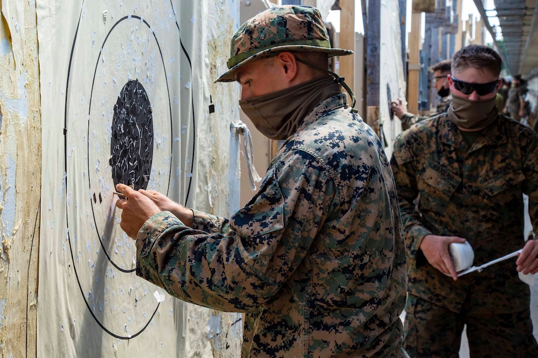 A Marine wearing a face mask marks a target on a poster.