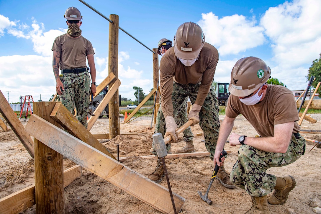 A sailor hammers in a stake as two others look on.