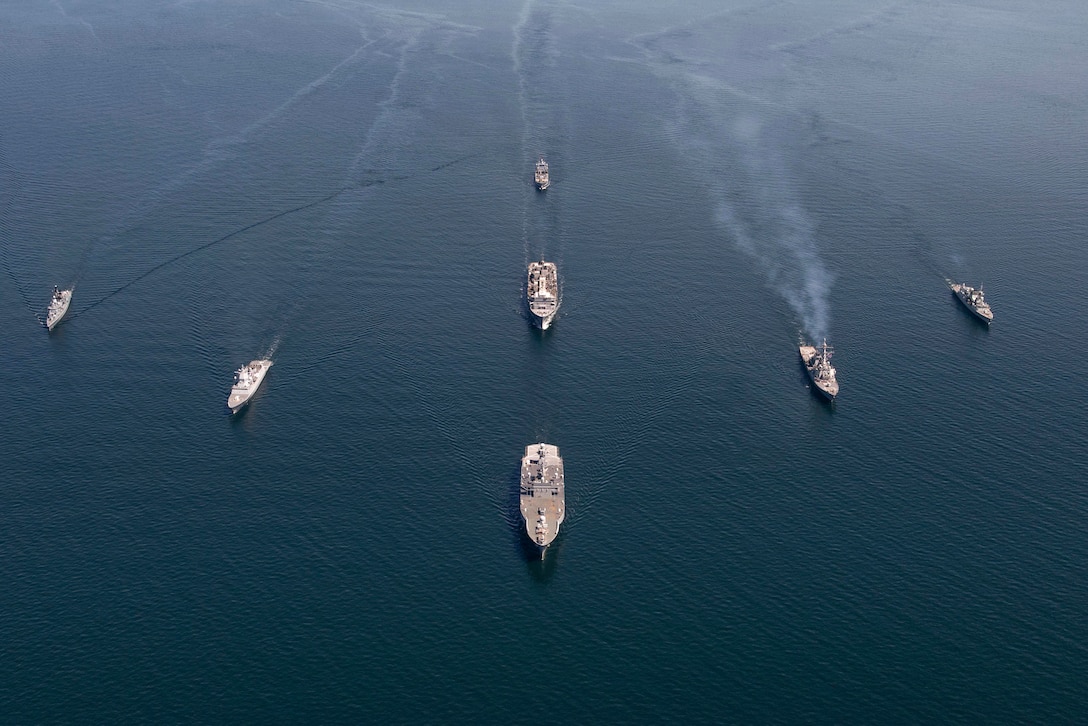 Seven naval ships from different nations transit a body of water.