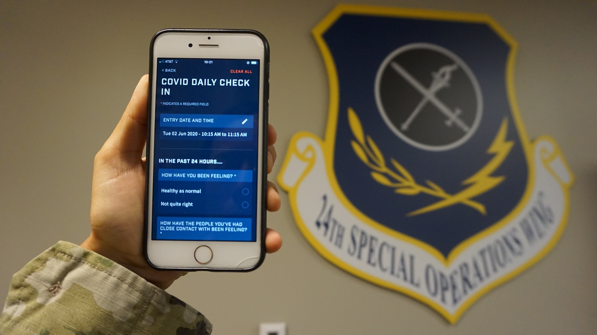 An Airman assigned to the 24th Special Operations Wing, holds up a smartphone with a dark blue unit shield reading 24th special operations wing in the background.