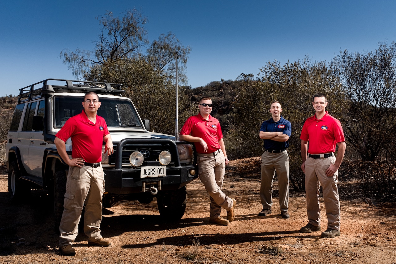 Four men pose beside an all-terrain vehicle in the desert.