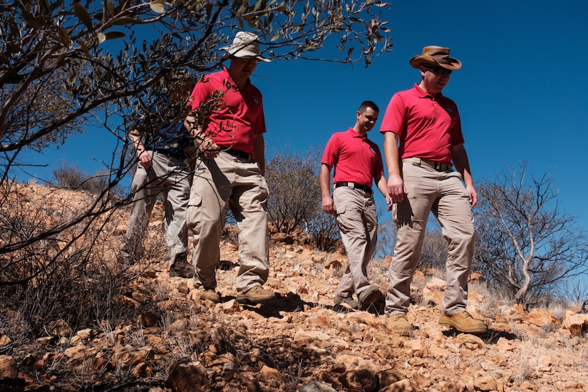 Four men in khakis and polo shirts walk down a rock-covered hill.