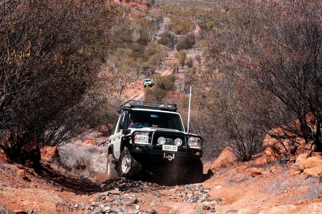 Two all-terrain vehicles navigate rocks on a dirt path in the desert.