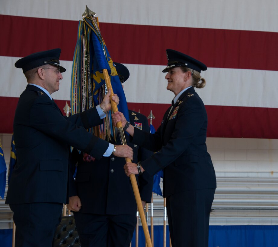 Two people standing on a stage in front of a flag.