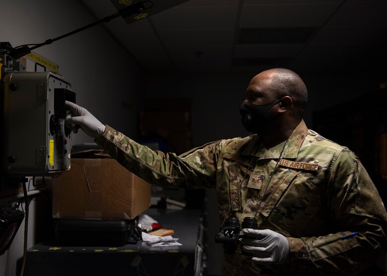 An Airman holding a pair of night vision goggles touches a test station for night vision goggles.