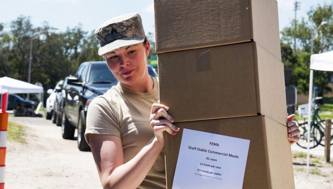A female National Guard soldier carries boxes of food and water in support of hurricane victims.