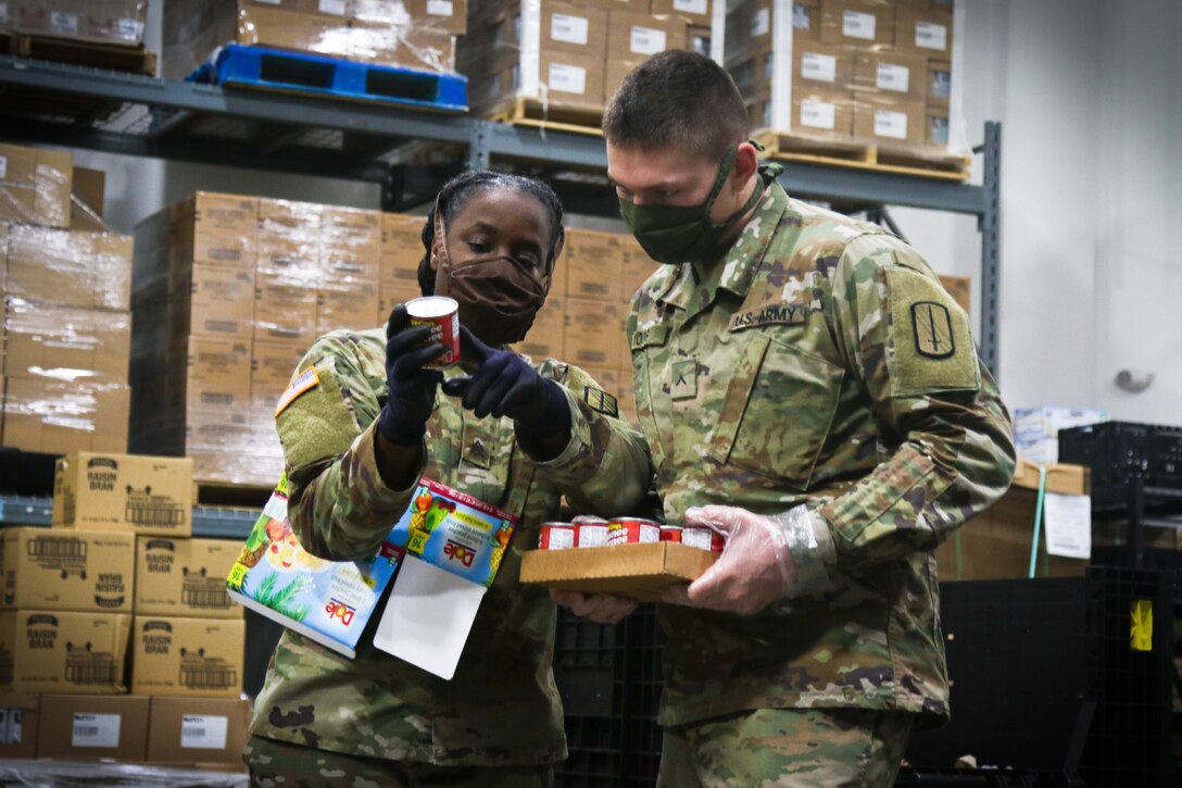 Two soldiers talk while holding containers of food.