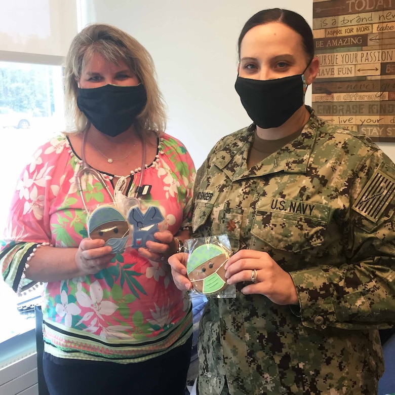 A woman in civilian clothes and a Navy officer in uniform, both wearing masks, pose for a photo.