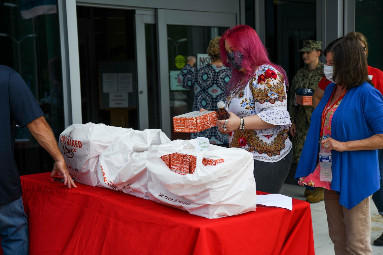 Two women wearing masks receive boxed lunches at an outdoor table.