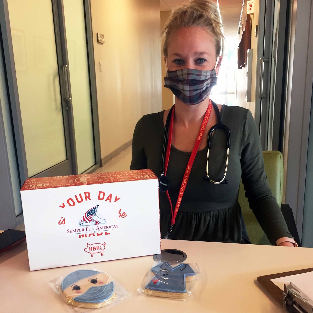 A woman wearing a mask poses with a boxed lunch and cookies.