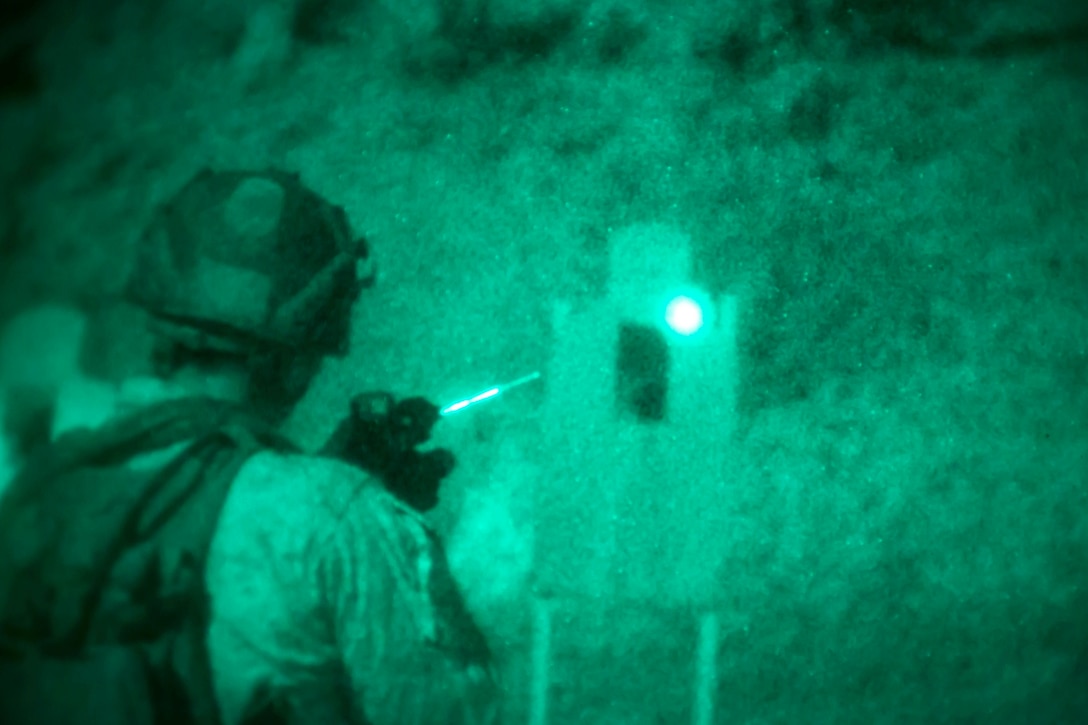 A Marine illuminated by green light fires a weapon at night.