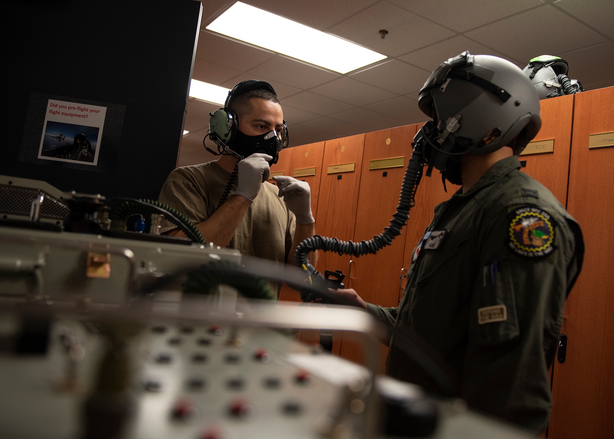 An Airman talks into a headset while another Airman wears a helmet and oxygen mask.