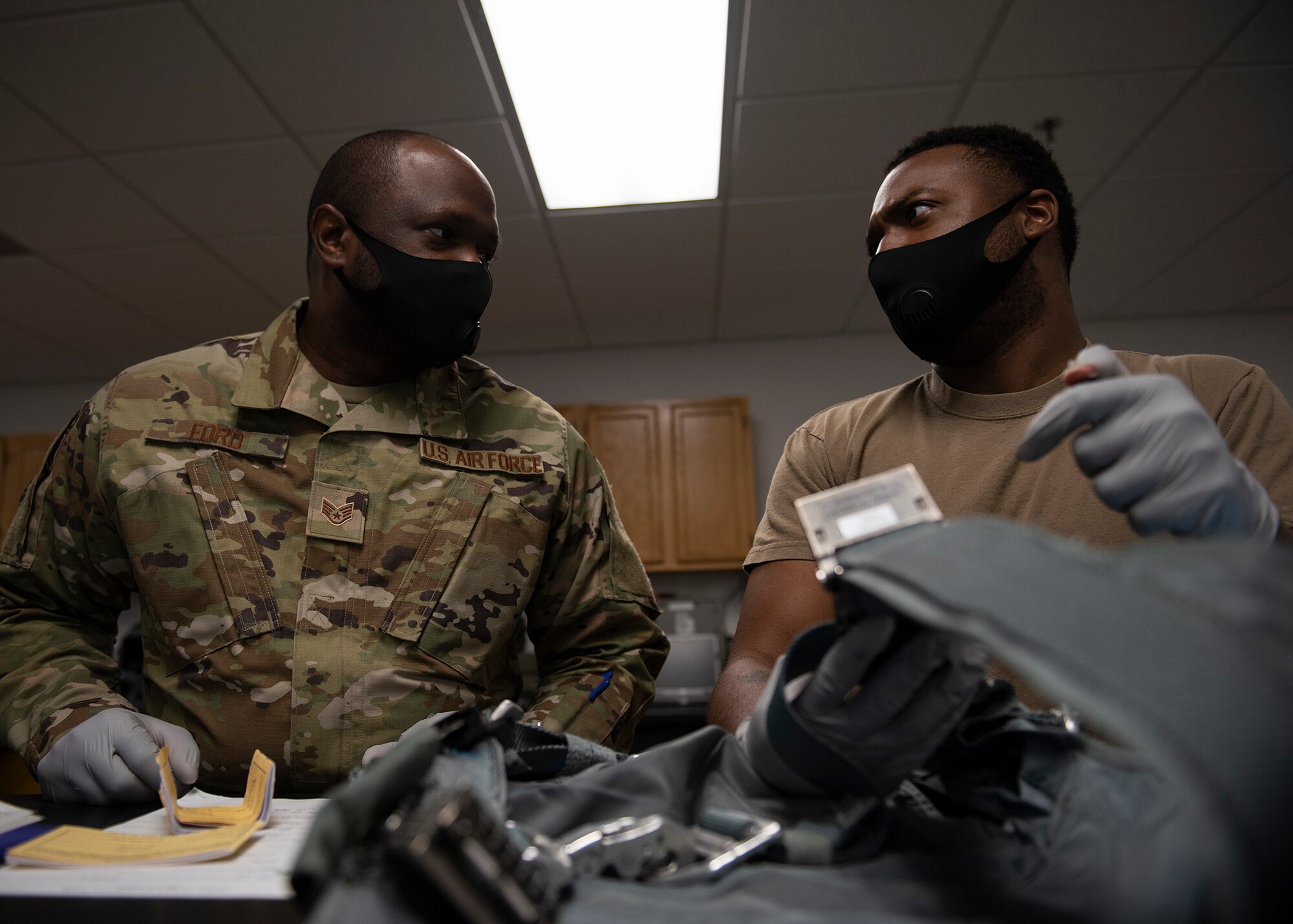 Two Airmen discuss the proper procedures to inspect a harness.