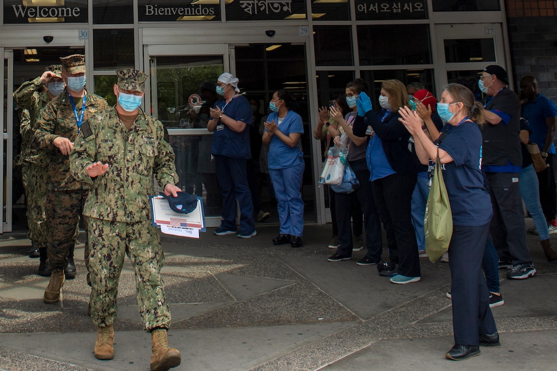 Medical staff wearing protective gear clap for sailors also wearing protective gear.