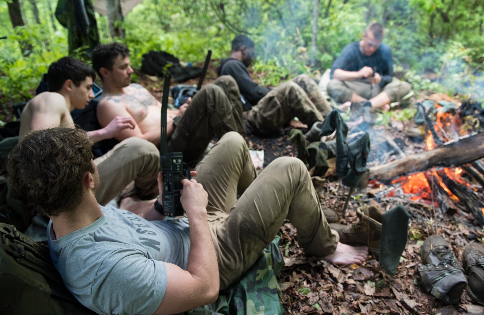 A group of Airmen dry themselves and their equipment by a fire on a mountain during combat survival training, near Brevard, North Carolina, May 21, 2020. It rained every day during the three-day CST, causing the steep, mountainous terrain to be muddier and more treacherous than normal. (U.S. Air Force photo by Senior Airman Kenneth Boyton)