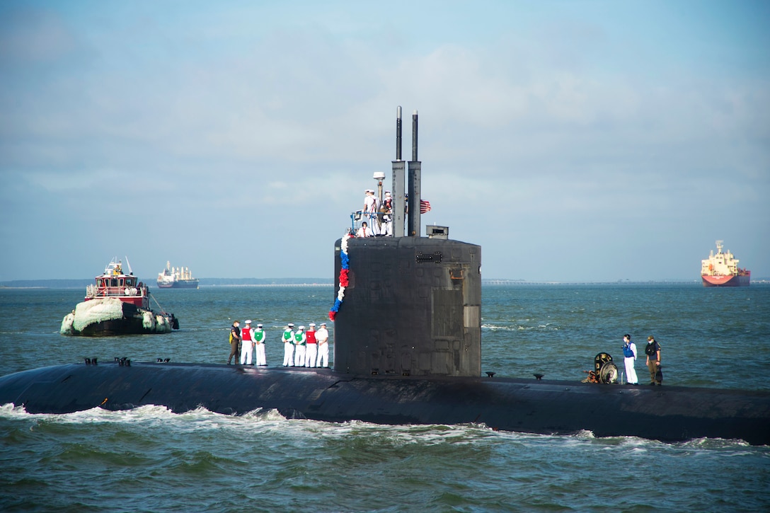 Sailors stand on a submarine surrounded by three other vessels.