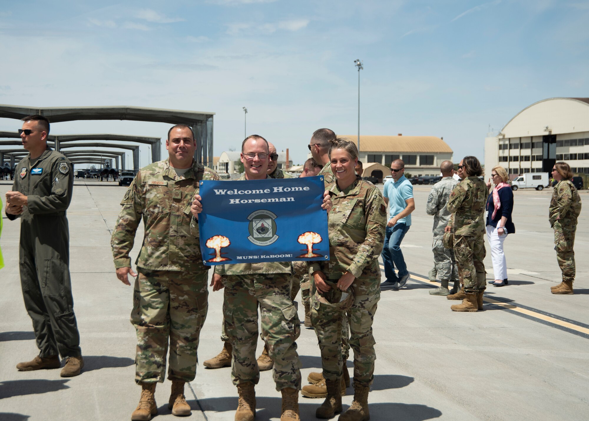 U.S. Air Force Master Sgt. Dan Hansen 366th Munitions Squadron first sergeant (left), Maj. Jonathan Hoefing 366th Munitions Squadron commander (mid), and 2nd Lt. Callie Welch 366th Munitions Squadron flight commander (right) pose for a photo with a welcome home poster June 3, 2020, at Mountain Home Air Force Base, Idaho. The poster is for the return of the 389th Fighter Squadron after an 8-month long deployment. (U.S. Air Force photo by Airman 1st Class Akeem K. Campbell)