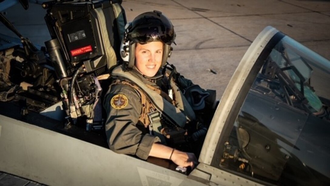 A Marine Corps pilot poses for a photo in an aircraft cockpit.