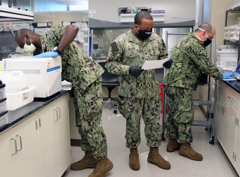 Three sailors wearing face masks work in a lab.