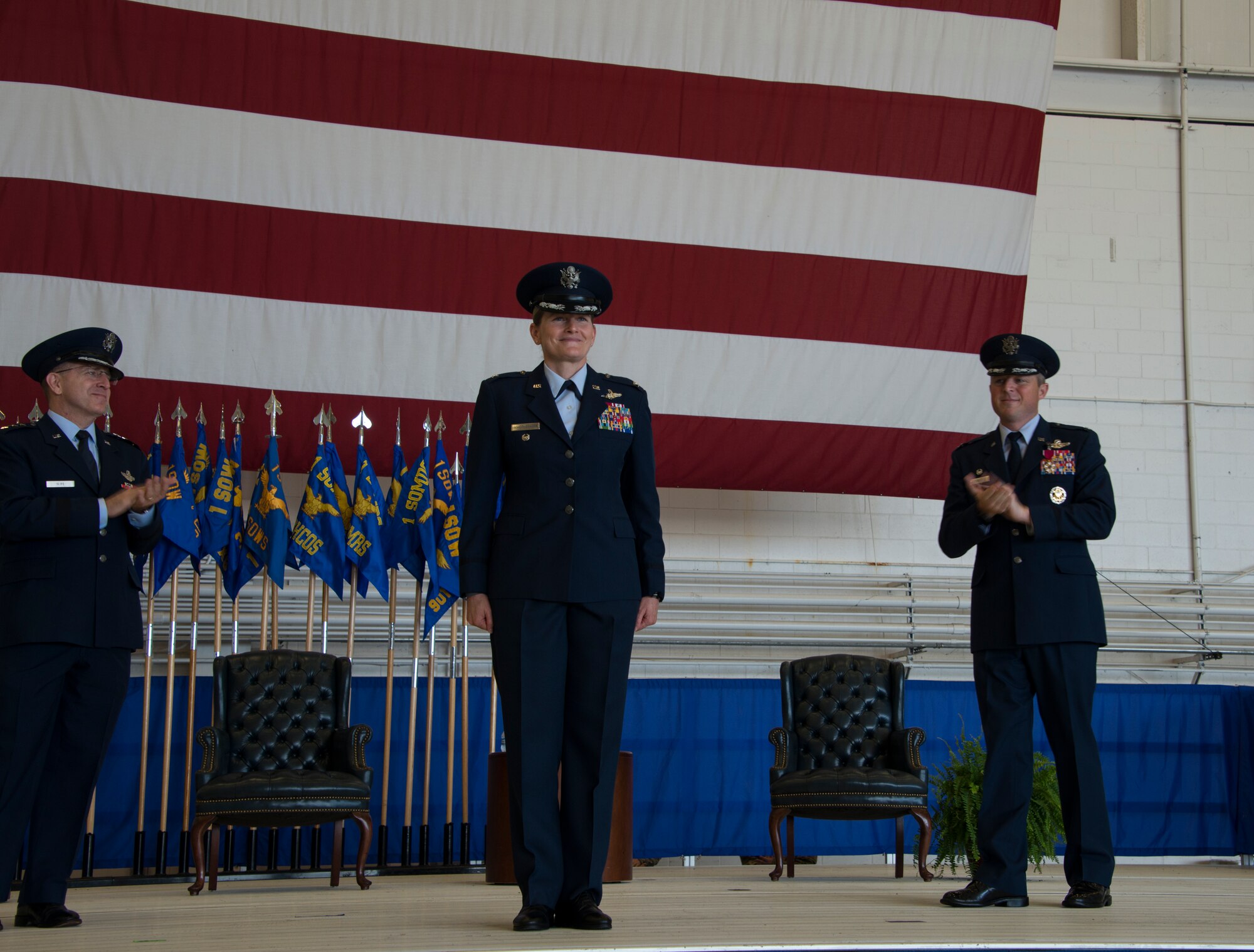 Three people standing on a stage in front of a flag.