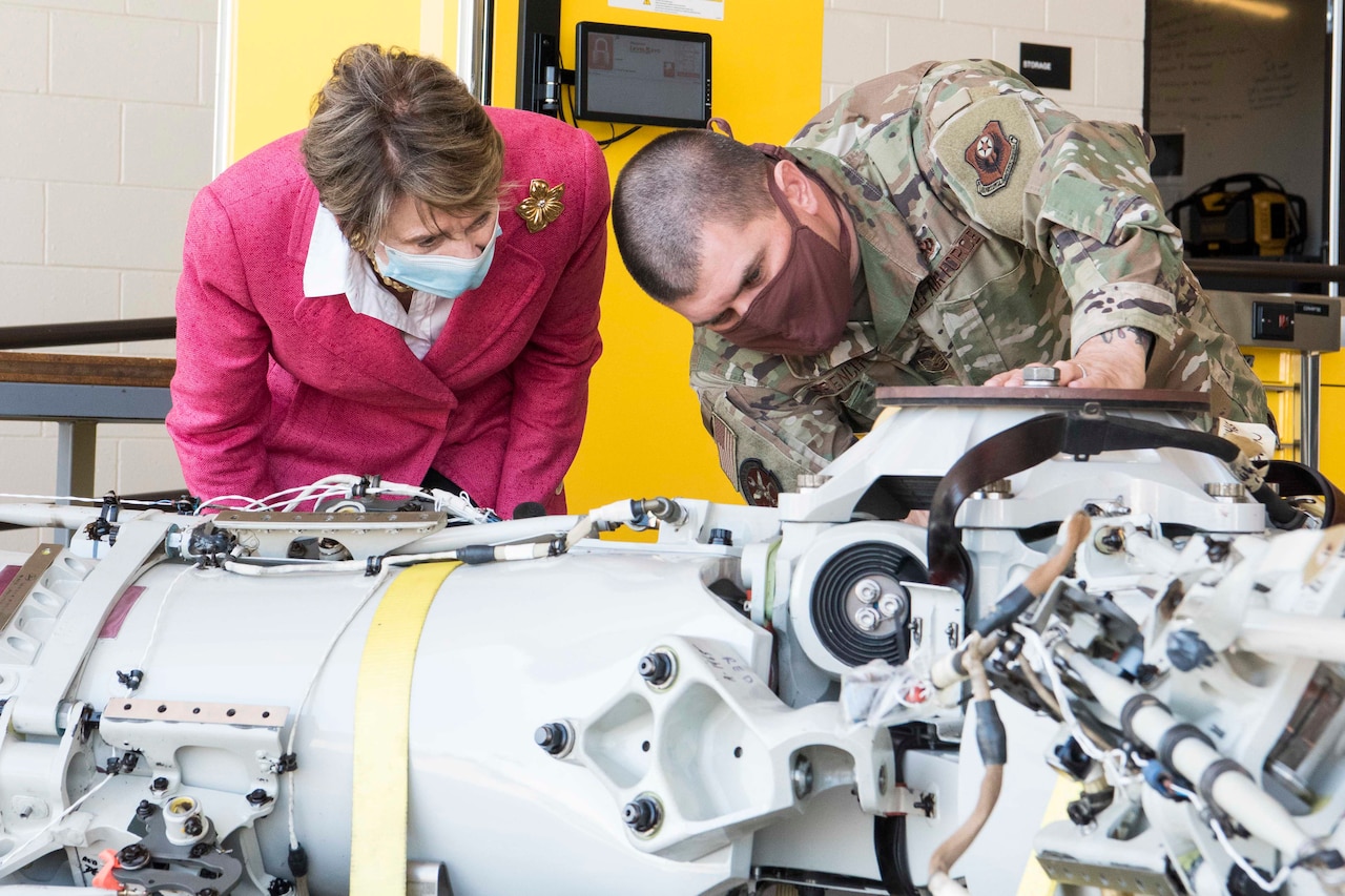 Air Force Secretary and a maintenance airman take a close look at aircraft parts. Both are wearing face masks.